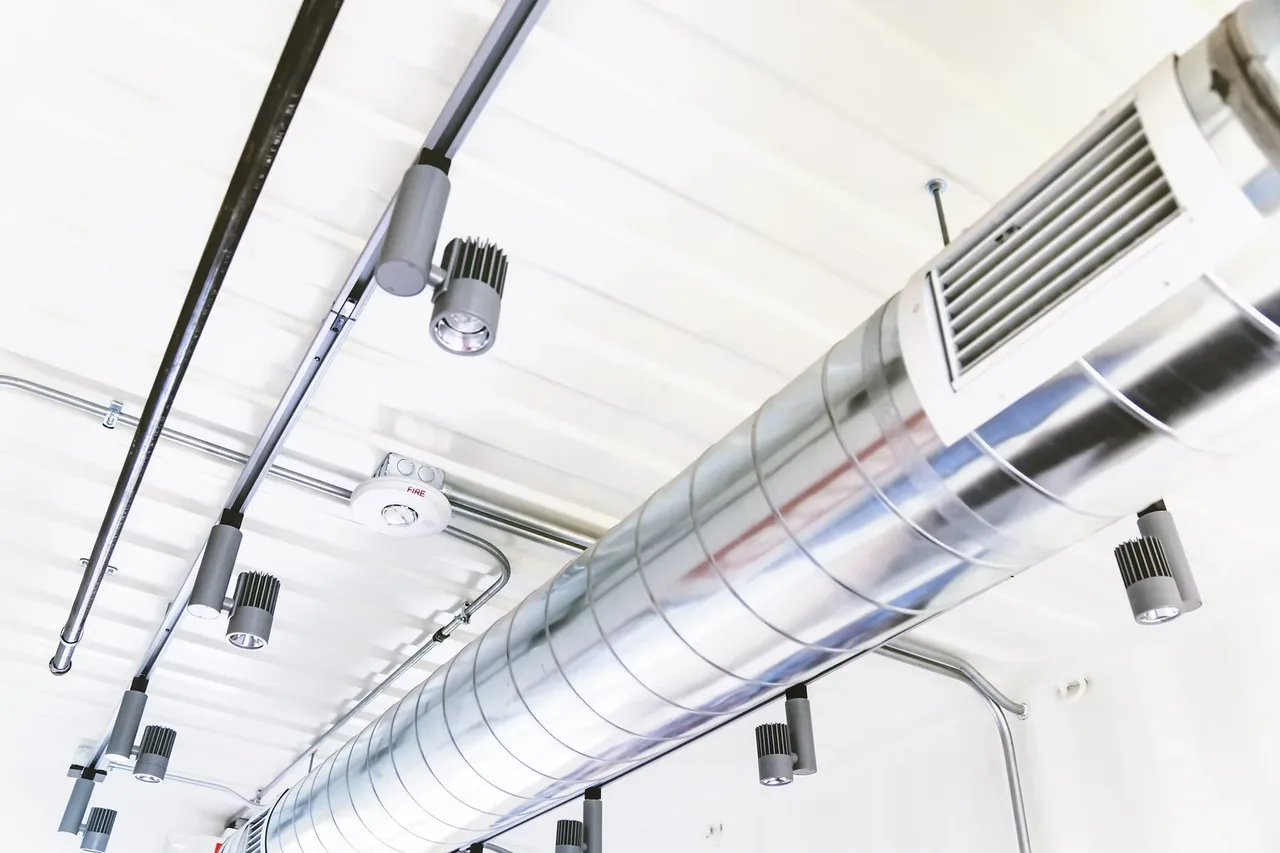 Exposed spiral ductwork and track lighting across a white ceiling